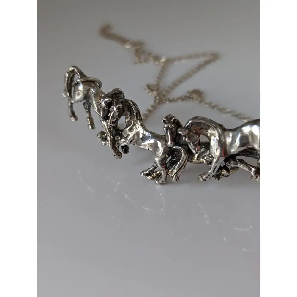 Silver steed herd necklace featuring a silver necklace with a sculpted pendant of horses in motion