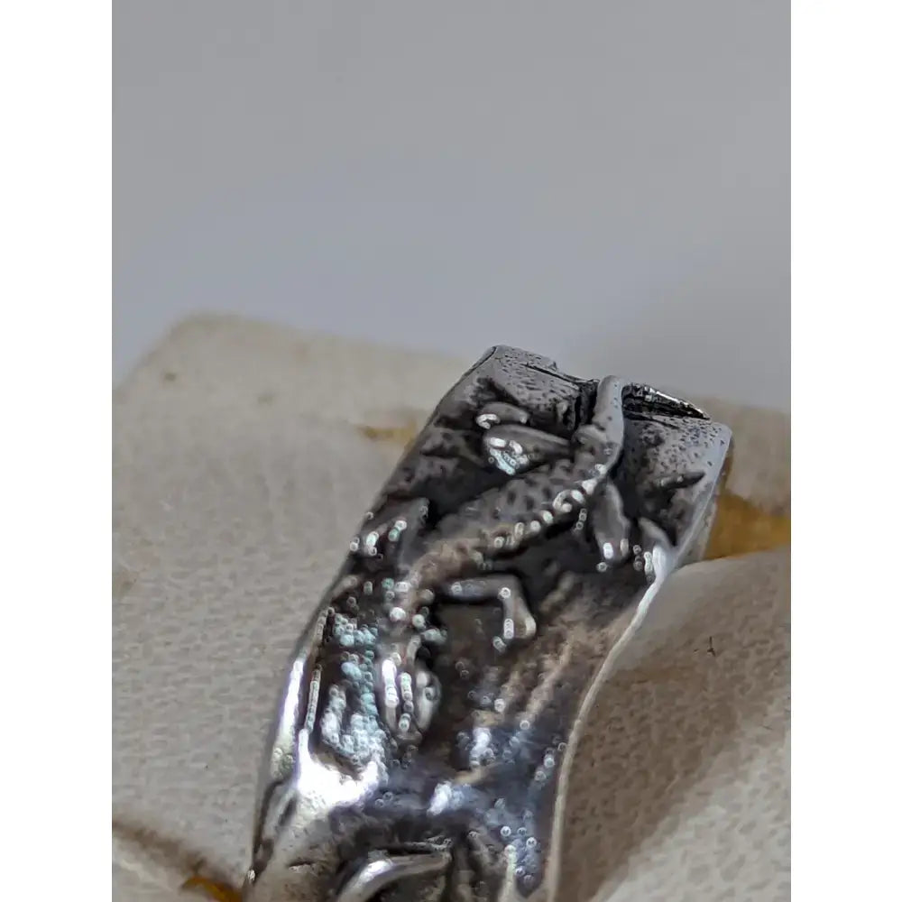 Silver steed lizard band is a silver-toned ring with a detailed textured design of two frogs in mid-leap
