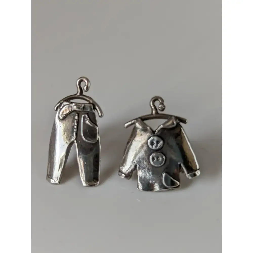 Silver steed pajama stud earrings featuring silver metal charms shaped like jeans and a button-up shirt hanging on hooks