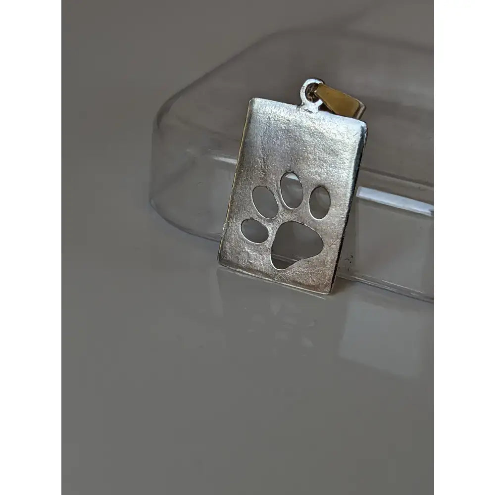Silver pendant silver steed paw with a textured matte finish and cut out paw print tag design with gold bail