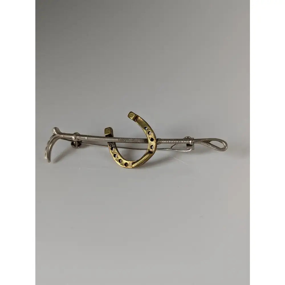 A sleek two-tone metal stock tie pin with a silver steed shoe and a gold cane gold brooch design