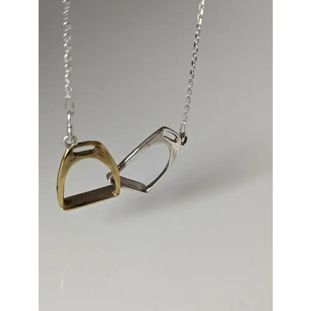 A delicate silver steed equestrian jewelry two stirrups necklace with one gold and one silver pendant on a fine chain