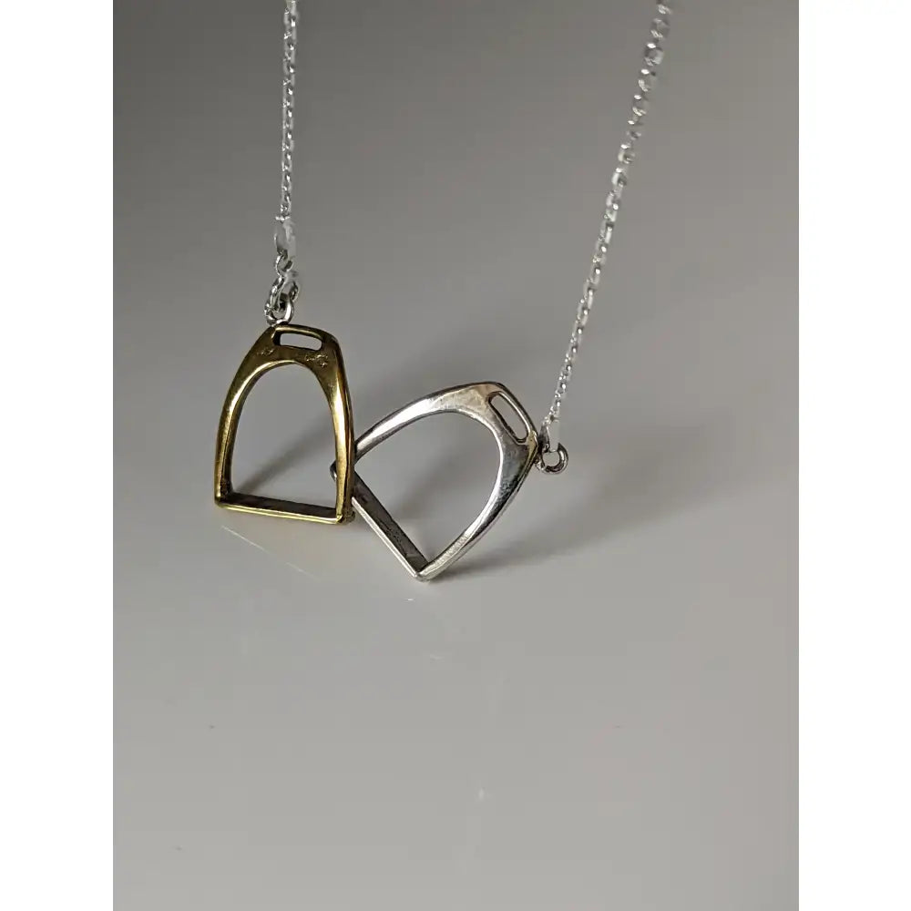 A delicate silver steed two stirrups necklace with gold and silver interlocking pendants on a fine chain