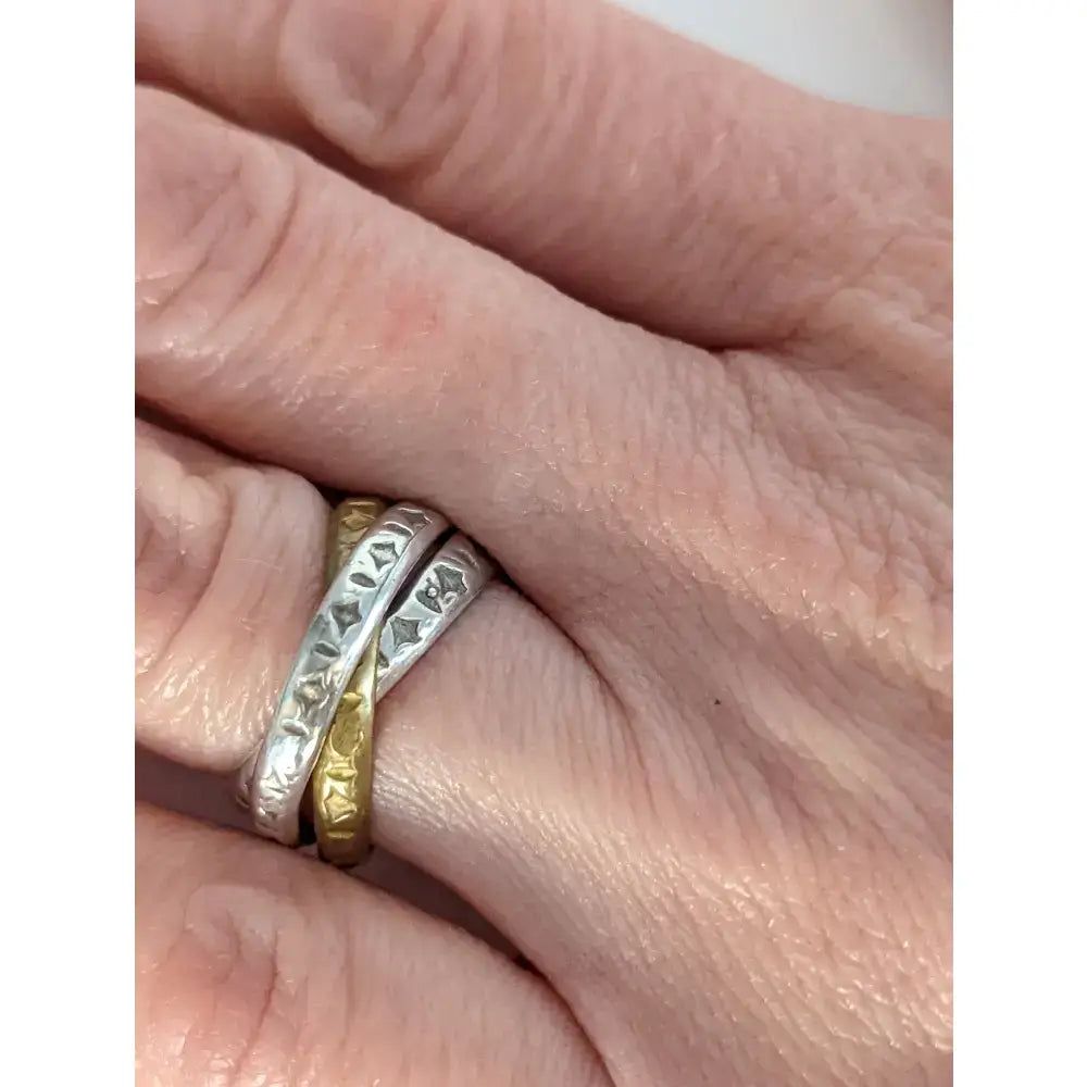 A silver steed two tone ring featuring three interlinking bands in silver textured diamond and gold worn on a finger