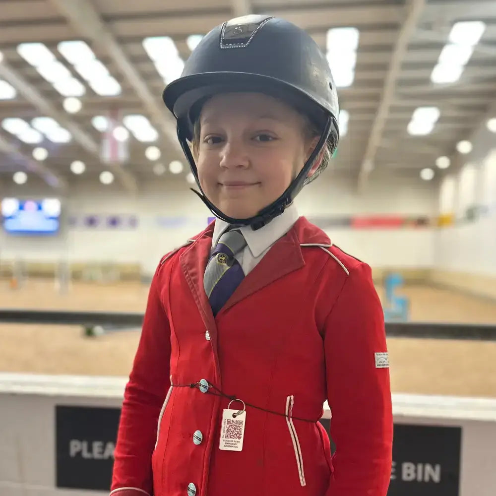 Red equestrian jacket with white trim and silver buttons featured on small rider emergency tag for young riders and pony club