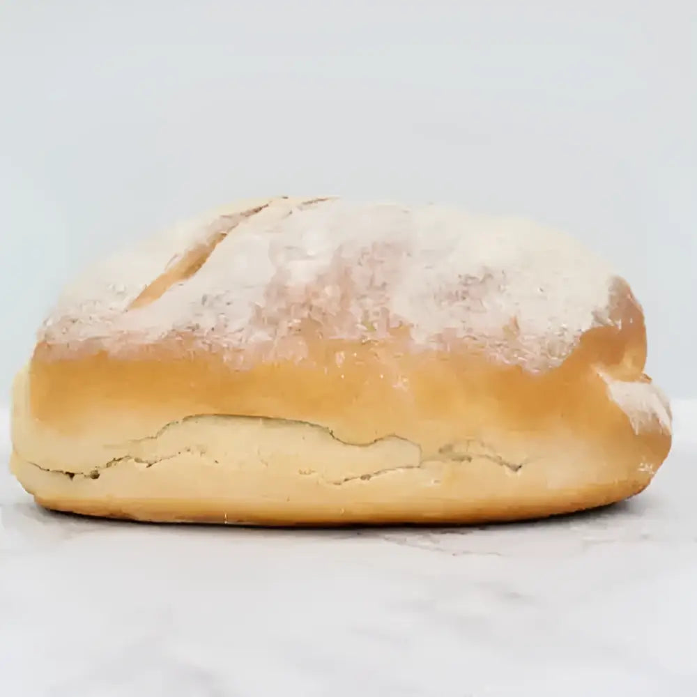 Golden-brown sourdough wholemeal bread with a rustic cracked crust and flour dusting on round white bread loaf