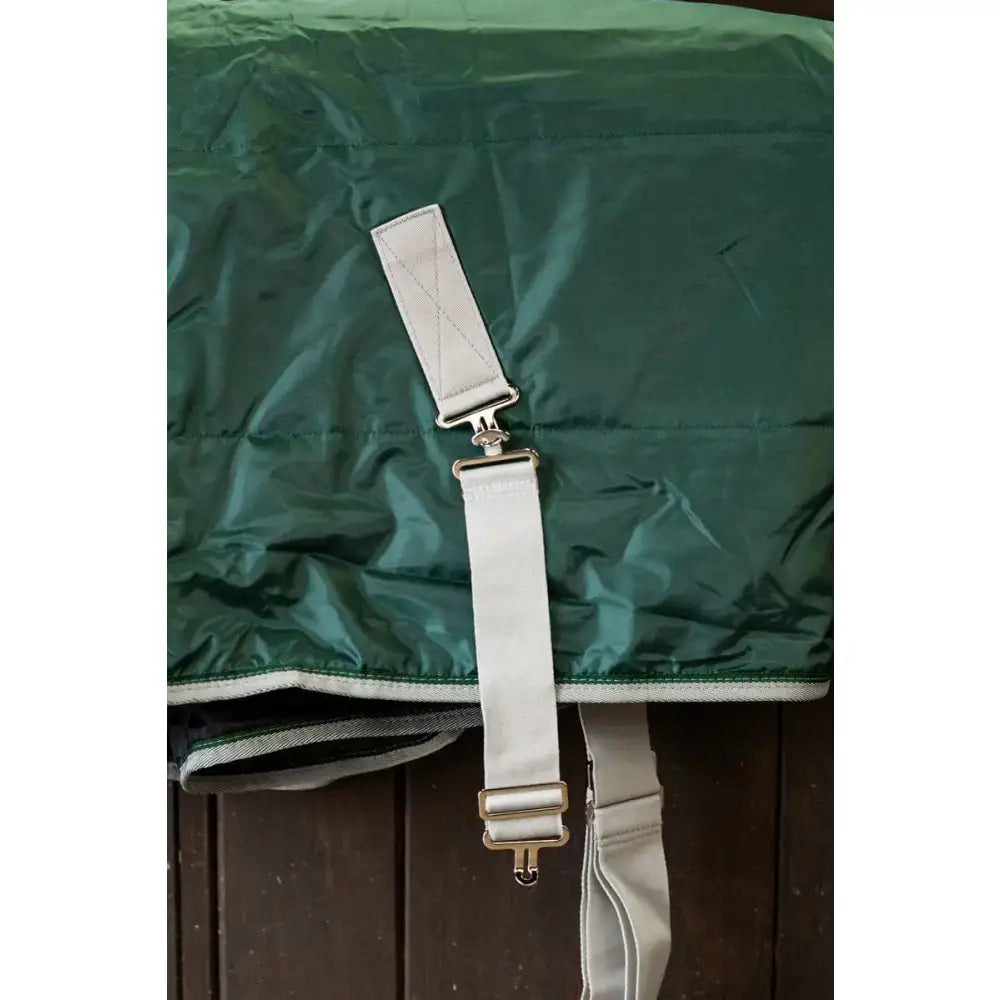White adjustable surcingle extenders with silver metal hardware attached to green fabric for equestrian horses