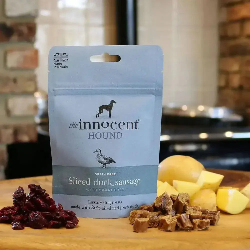 A light blue pouch of innocent hound sliced duck sausage dog treats with cranberry and black branding