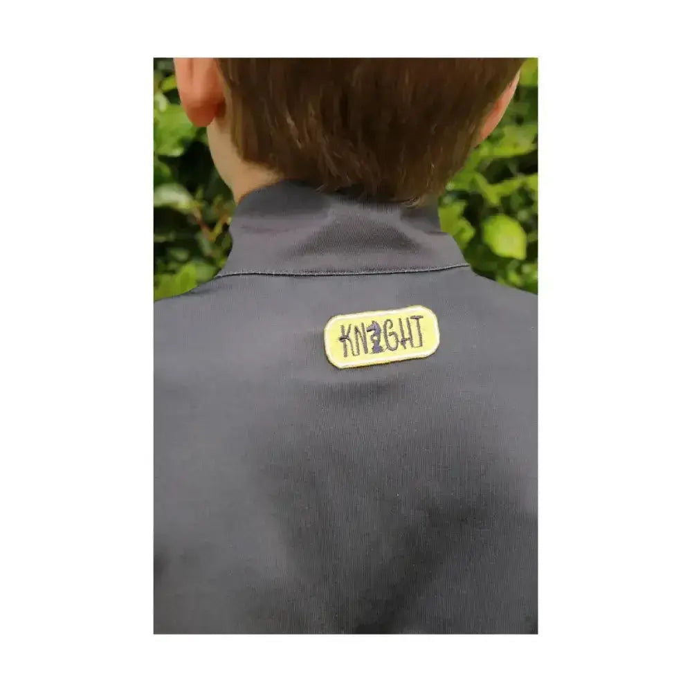 A pale yellow knight patch embroidered on a charcoal grey base layer jacket from little knights tractor collection base