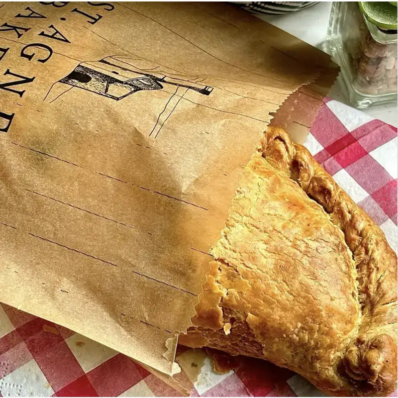 Golden brown flaky traditional steak pasty peeking from a brown paper bag from pasty st anges bakery