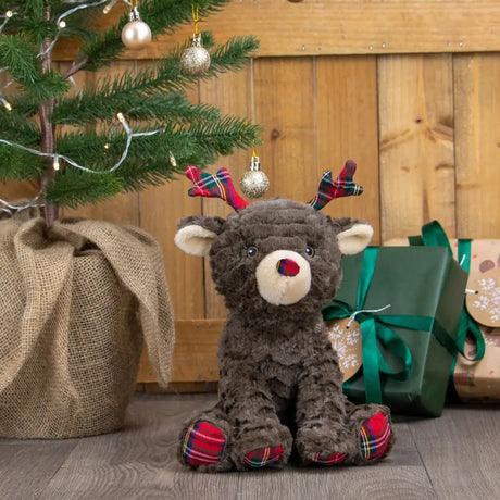 A plush brown ancol dorothy doe reindeer with white muzzle red nose and plaid antlers in a festive holiday setting
