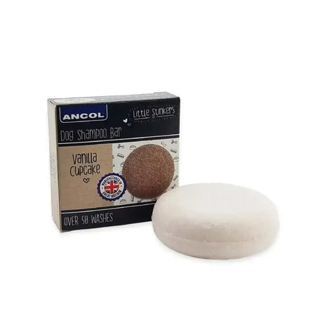 A white round stinkers dog shampoo bar with a smooth surface sits beside its vanilla cupcake packaging