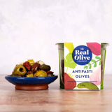 A colorful square tin of the real olive company antipasti olives with vibrant green and pink botanical label and stuffed green olives