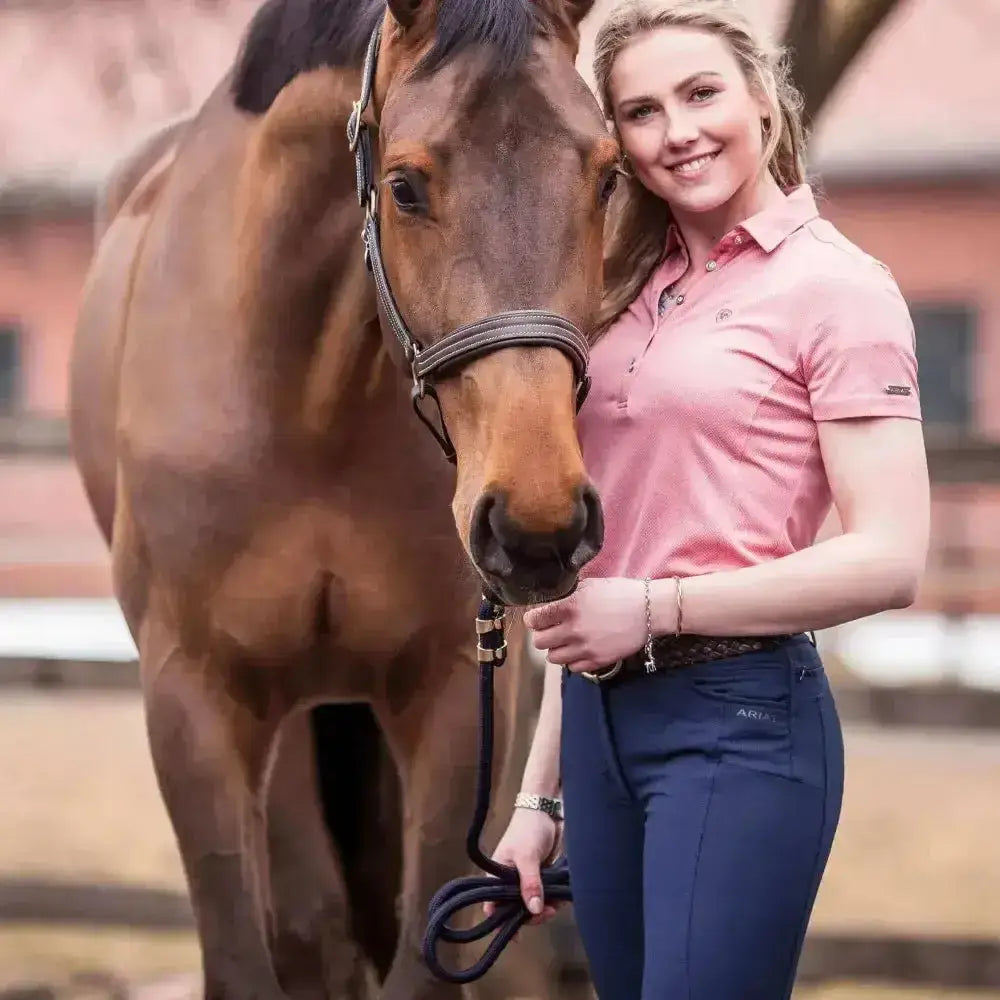 A woman stands with a brown horse wearing ariats pink prelude riding breeches with four-way performance stretch fabric