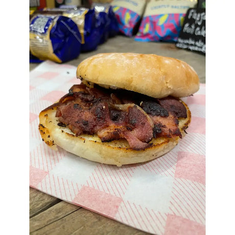 A bacon bap with a golden wheat flour bun filled with crispy coated skin bacon slices and charred edges