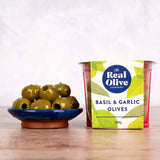 A vibrant blue ceramic bowl filled with glossy green basil and garlic olives packed in cold-pressed sunflower oil