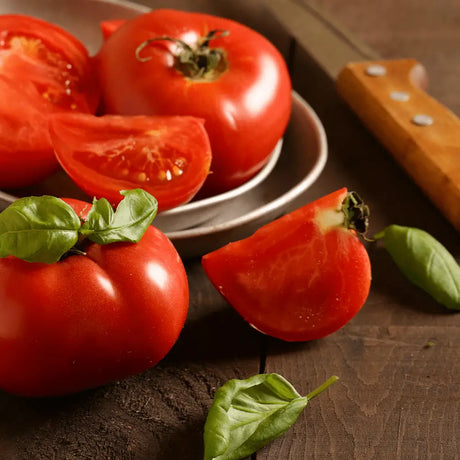 Fresh beef tomatoes with vibrant red glossy skin and green basil leaves, perfect alternative to large vine tomatoes