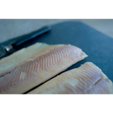 Two pale skinless fillets of blakewell smokehouse devon hot smoked rainbow trout on a dark cutting board
