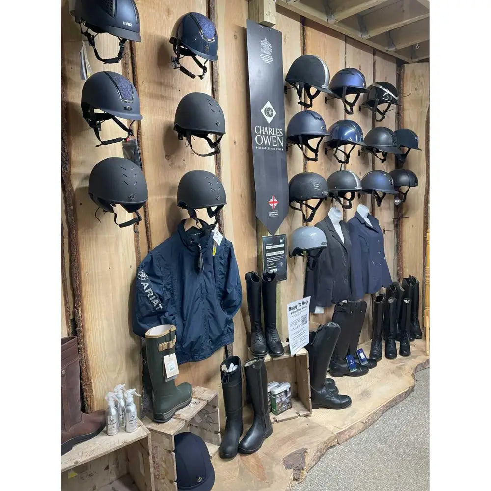 Black charles owen equestrian helmet on wooden wall rack for booking a fitting appointment with horses in mind