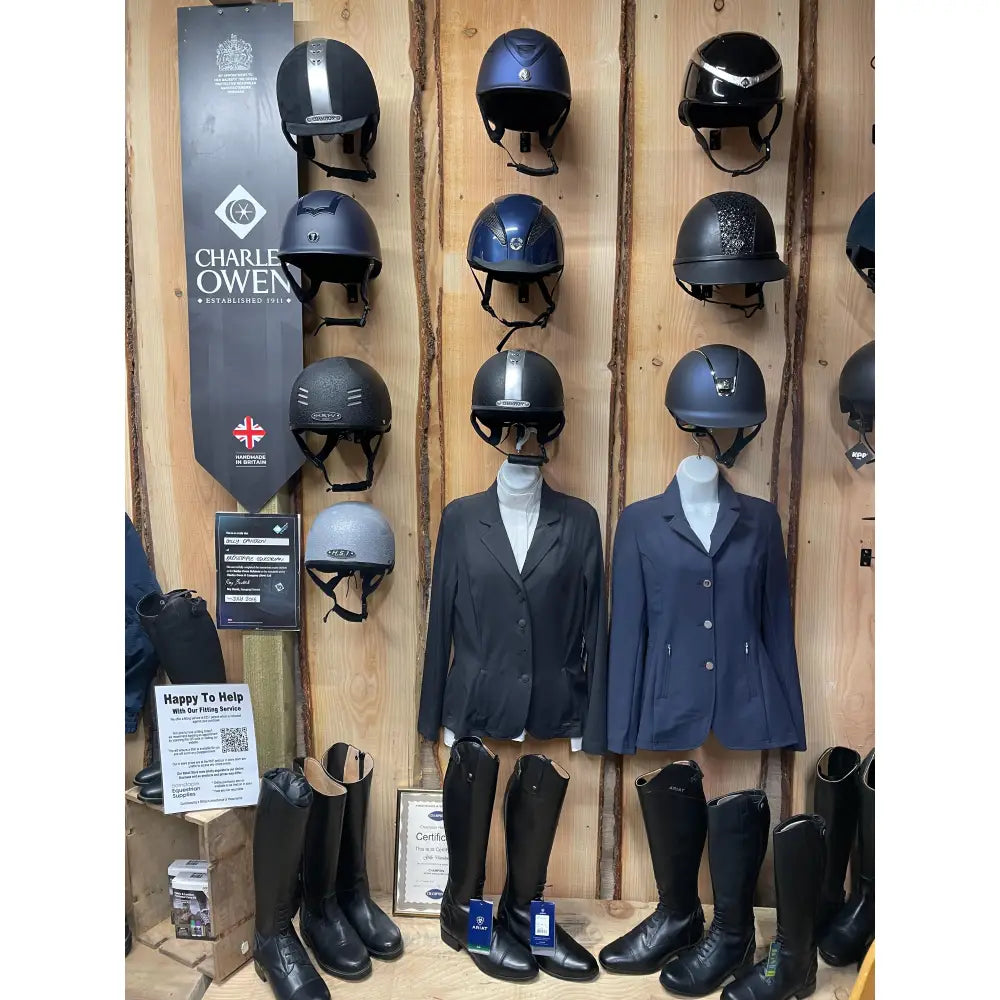 Black charles owen equestrian helmets displayed on a wooden wall for booking a fitting appointment with horses