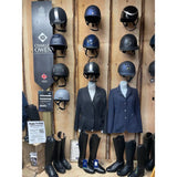 Black charles owen equestrian helmets displayed on a wooden wall for booking a fitting appointment with horses