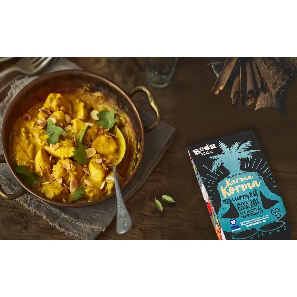 A vibrant yellow karma korma curry in a rustic copper pot garnished with cilantro and almonds from boom kitchen karma
