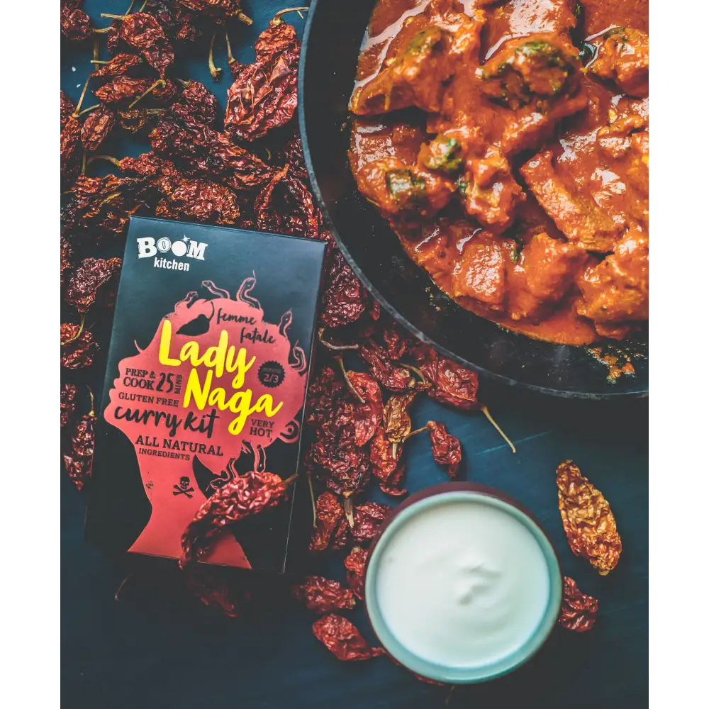 A vibrant red and black boom kitchen lady naga vindaloo curry kit box with bold yellow lettering and stylized design