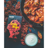 A vibrant red and black boom kitchen lady naga vindaloo curry kit box with bold yellow lettering and stylized design