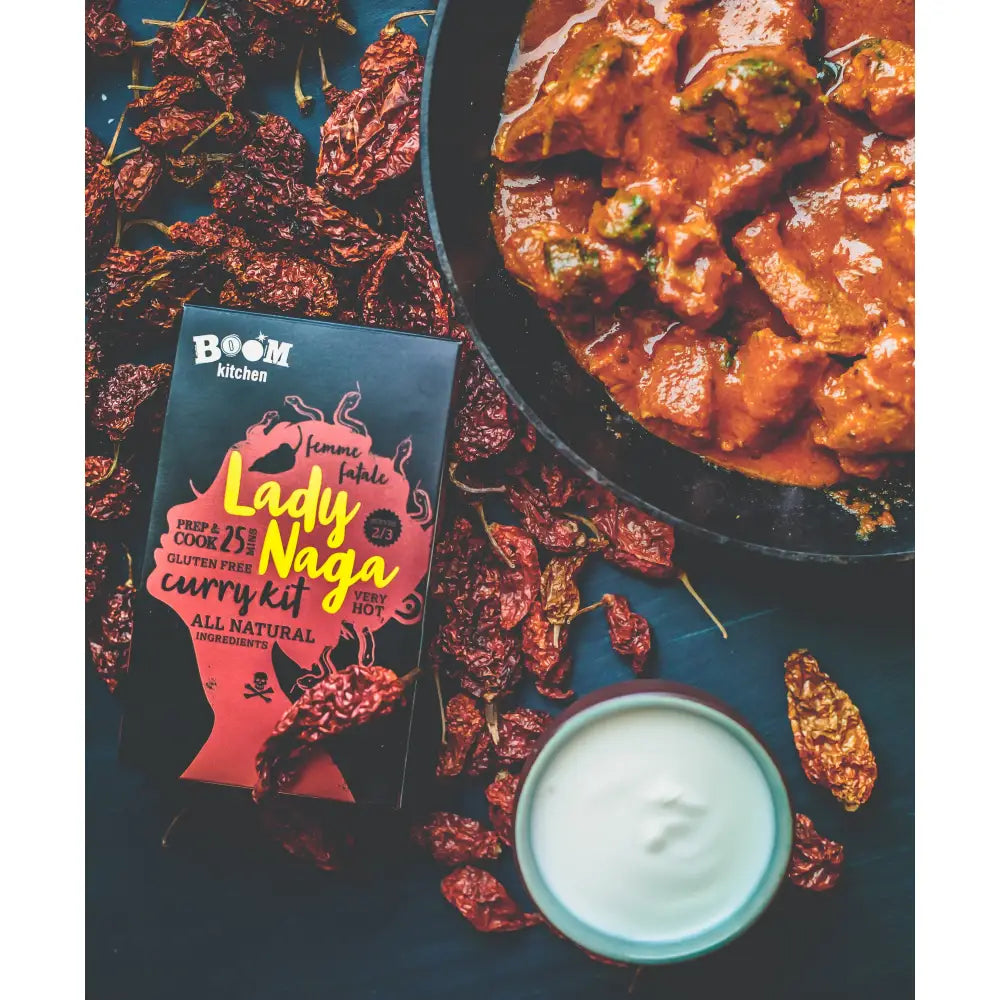 A vibrant red and black boom kitchen lady naga vindaloo curry kit box with bold yellow lettering and stylized design