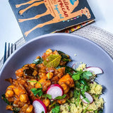 A vibrant yellow chickpea curry served with couscous and fresh cilantro in a boom kitchen mellow moroccan bowl