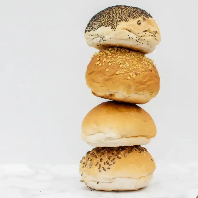 Stack of golden brown bread rolls packs topped with black poppy sesame and mixed seeds in round white bread style