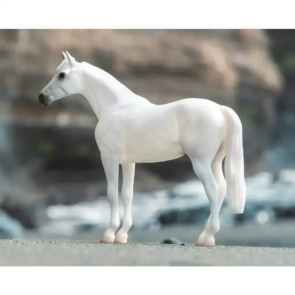 A sleek all-white plastic breyer fleabitten grey thoroughbred model horse with detailed muscles and a glossy finish