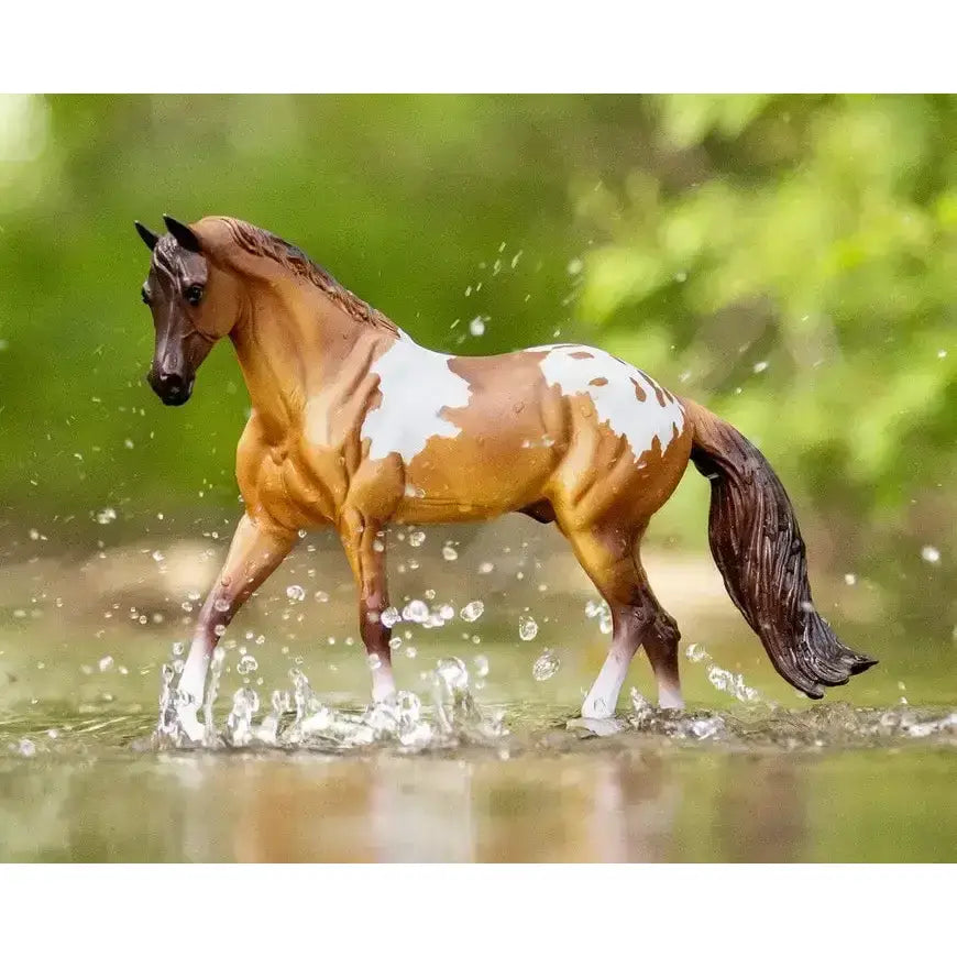 A detailed breyer red dun pintaloosa model horse with tan and white spotted coat standing in shallow water