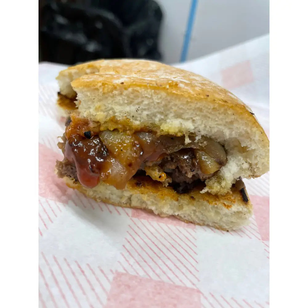 A juicy burger bap with a glossy reddish brown sauce and caramelized onions on golden wheat flour buns