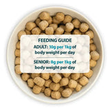 Tan round kibble pellets of burns original lamb dog food by john burns in a white bowl with feeding guide visible