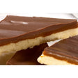 A caramel shortcake slice with glossy dark chocolate topping over caramel and golden shortbread in airtight container