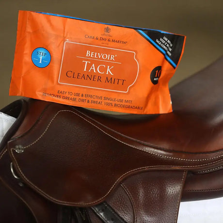 Orange carr & day martin belvoir step 1 cleaning mitt resting on brown leather saddle for tack care