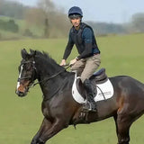 A dark brown horse with a white blaze wearing black tack and a white saddle pad featuring airways training with the groundbreaking charles owen pro 11 plus riding hat