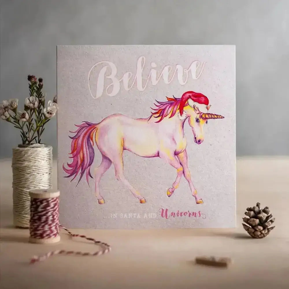A soft pastel unicorn christmas card on textured board with santa and unicorns theme and eco kraft fleck details