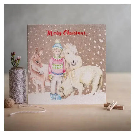 A festive beige eco kraft fleck christmas card merry with a child in a colorful sweater and donkeys in snow
