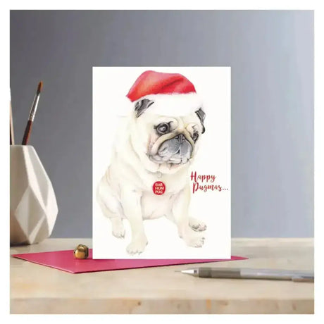 Christmas card rosa with a white pug illustration wearing a red santa hat and happy pugmas text on eco kraft fleck paper