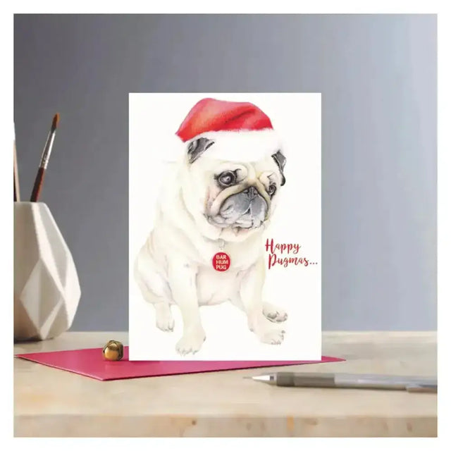 Christmas card rosa with a white pug illustration wearing a red santa hat and happy pugmas text on eco kraft fleck paper