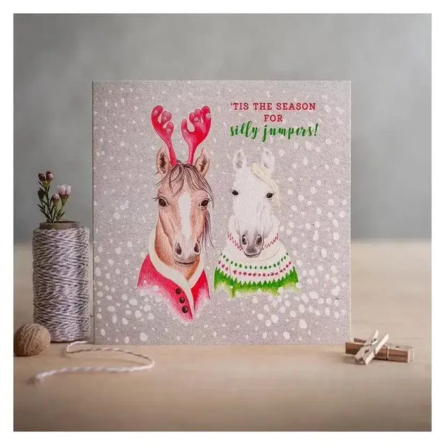 A christmas card season design with two horses in festive jumpers on an eco kraft fleck textured board background