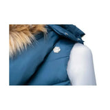 A silver hexagonal pin with an engraved design on the front of a cool slate blue coldstream leitholm quilted gilet
