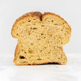 A slice of golden brown corn bread farmhouse loaf with airy interior and crust sprinkled with seeds