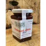 A glass jar of country markets damson jam with a white lid filled with dark red markets damson jam