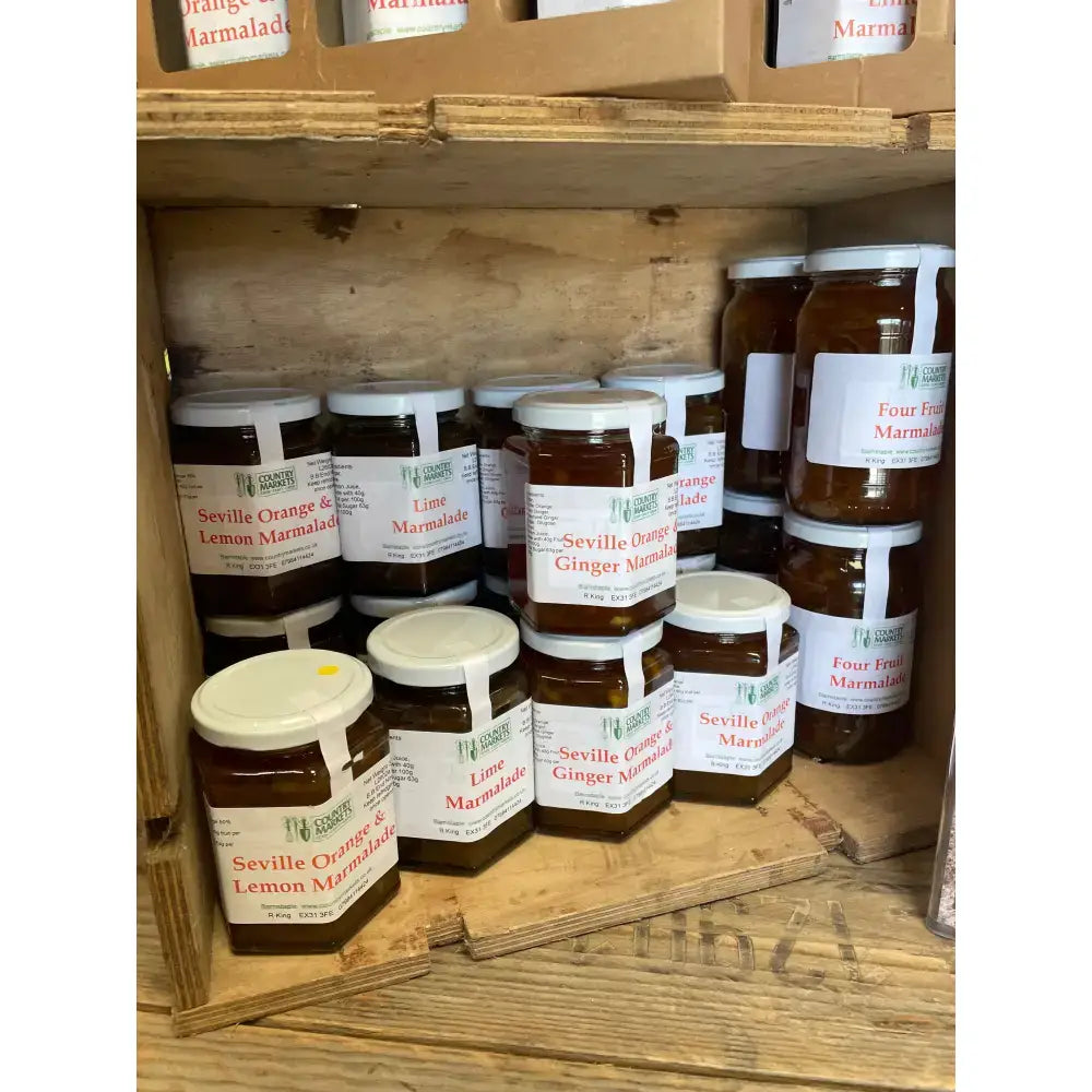 Hexagonal glass jars of amber four fruit marmalade sealed with white lids and labeled country markets four fruit