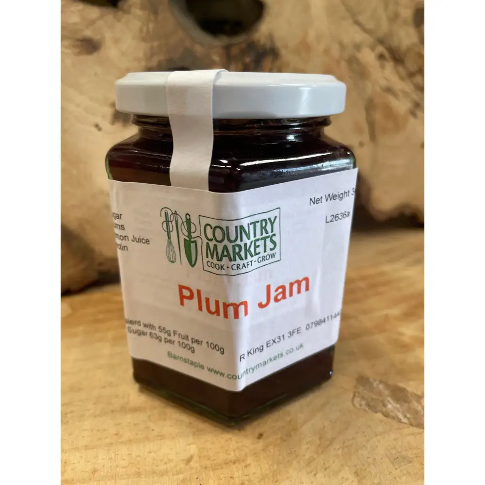 A glass jar of country markets plum jam with dark purple preserve and a white lid and label for sweet spreads