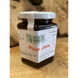 A glass jar of country markets plum jam with dark purple preserve and a white lid and label for sweet spreads