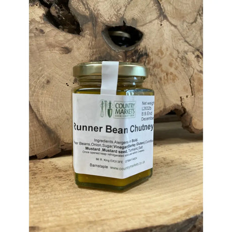 A glass jar of country markets runner bean chutney with a gold lid and white label filled with greenish yellow chutney
